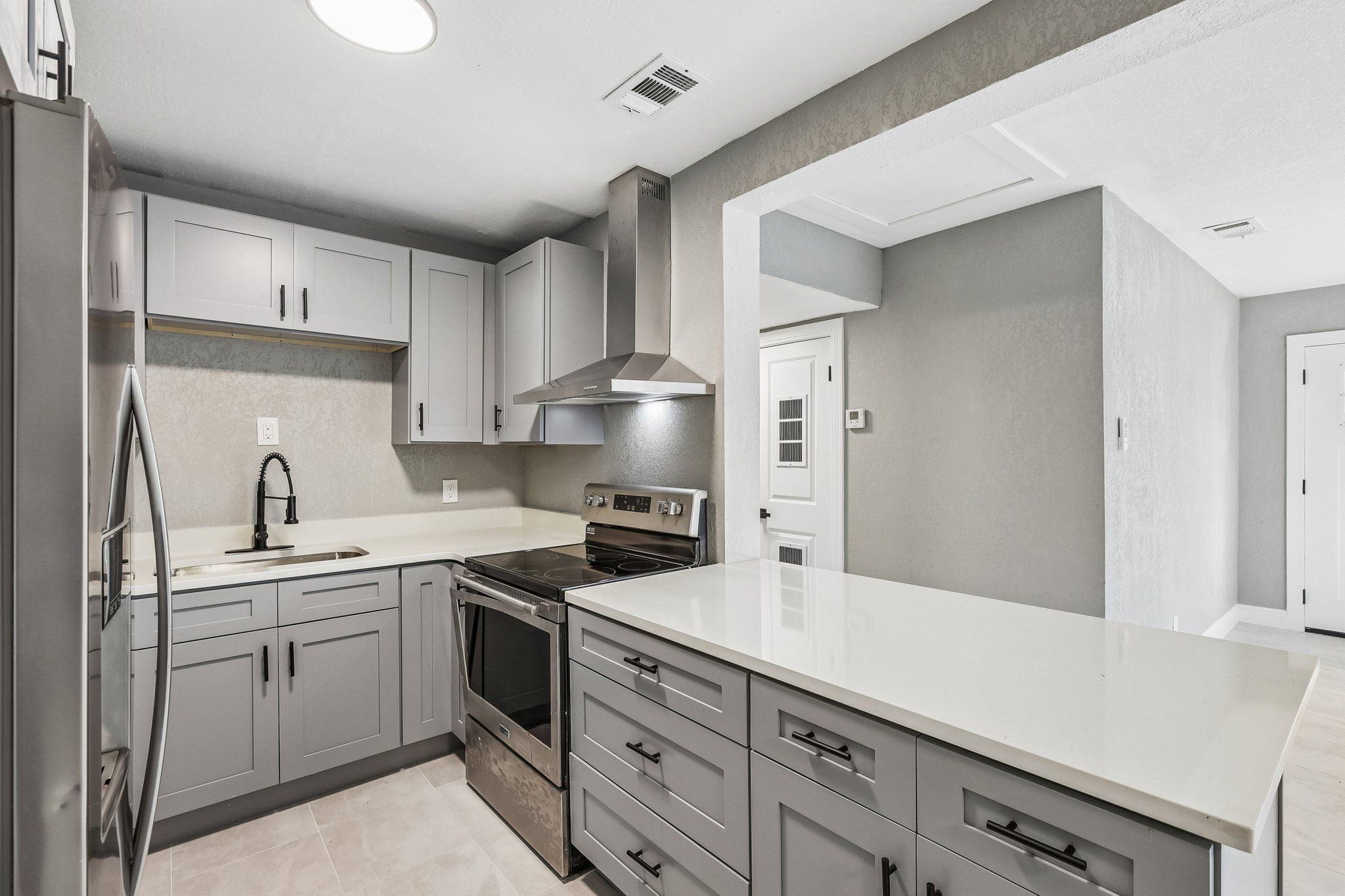Remodeled kitchen with gray shaker cabinets, quartz counters and stainless range