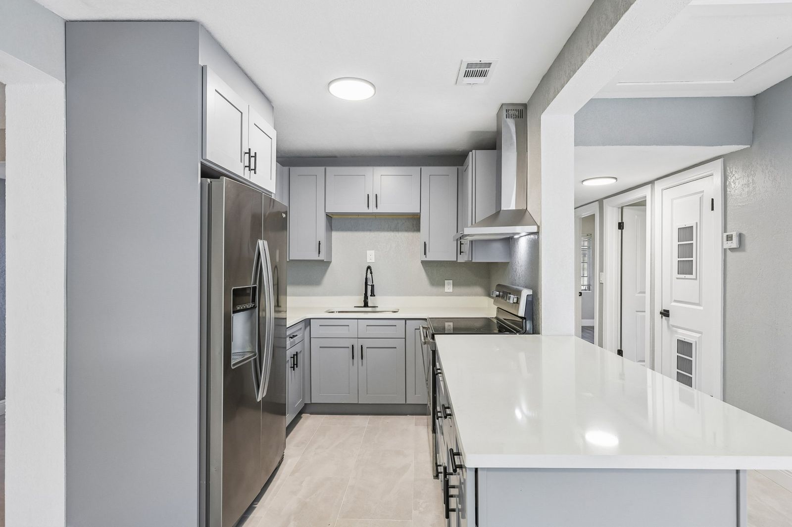 Mallory kitchen with stainless refrigerator, gray shaker cabinets and quartz island
