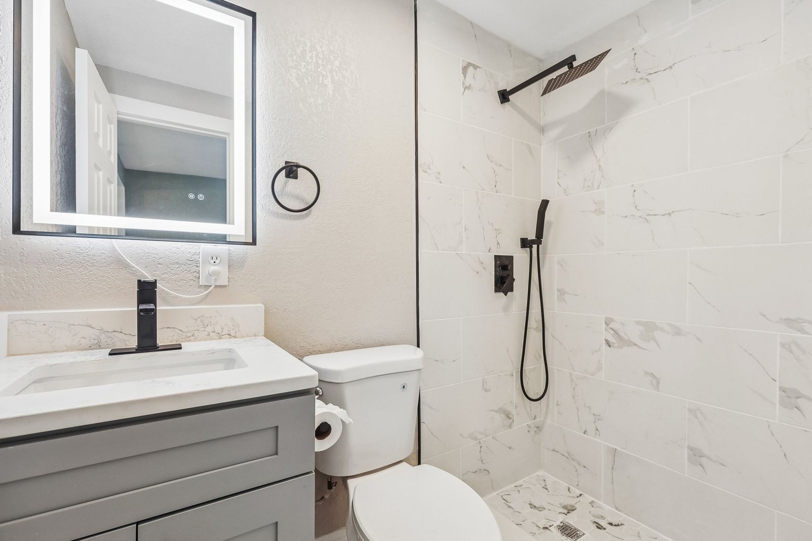 Remodeled bathroom with marble-look tile shower, gray vanity and LED mirror